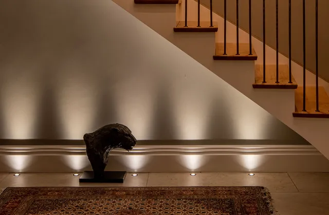 Bronze jaguar statue under stairs lit with floor recessed uplights