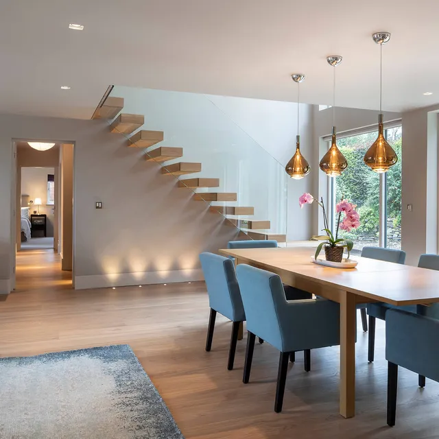 A bright airy dining room with uplighting under the cantilevered wooden staircase