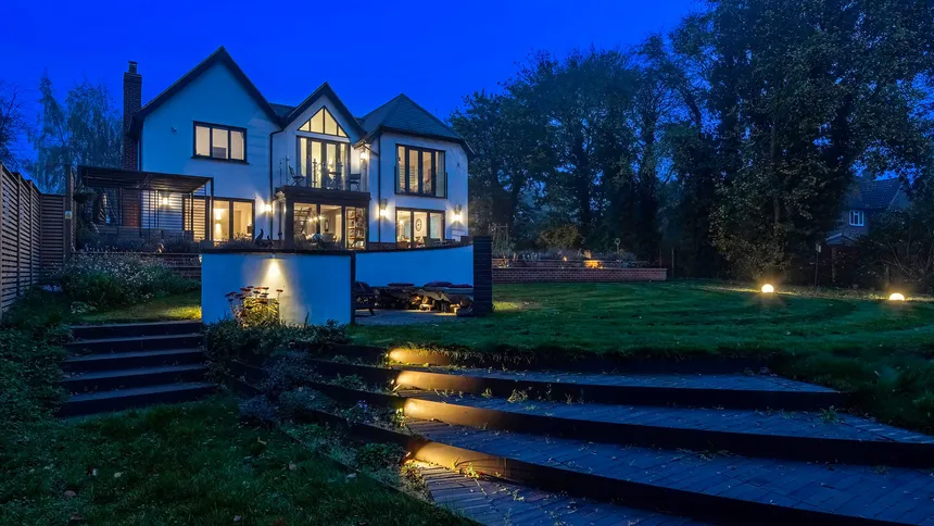 An autumnal garden at blue hour with lighting built into the stone steps and firepit. 