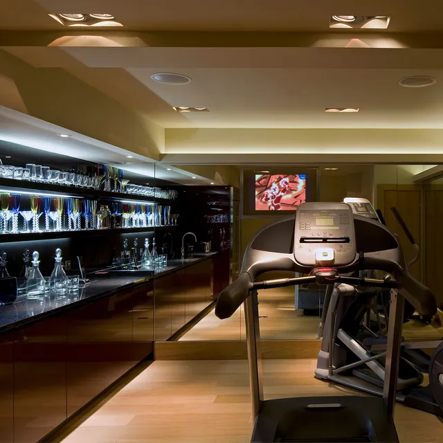 A small, well-stocked gym and bar with a mirror TV and ceiling speakers