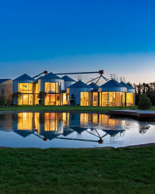 Evening shot of a luxury country house built around an array of agricultural silos