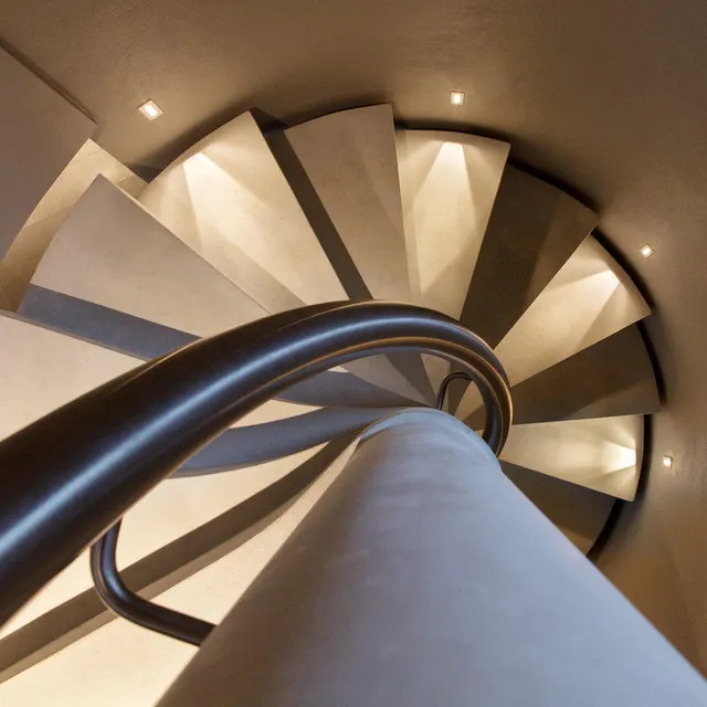 Top-down view of a spiral staircase lit with small, thin wall-mounted accent lights