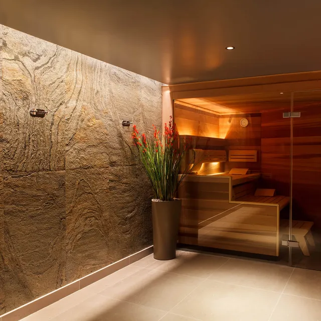 Linear LED lighting washes a textured tiled wall in a changing room with sauna