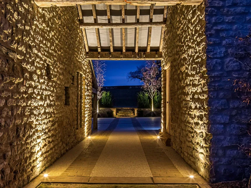 An uplit stone and timber beamed arch with a lit courtyard beyond.