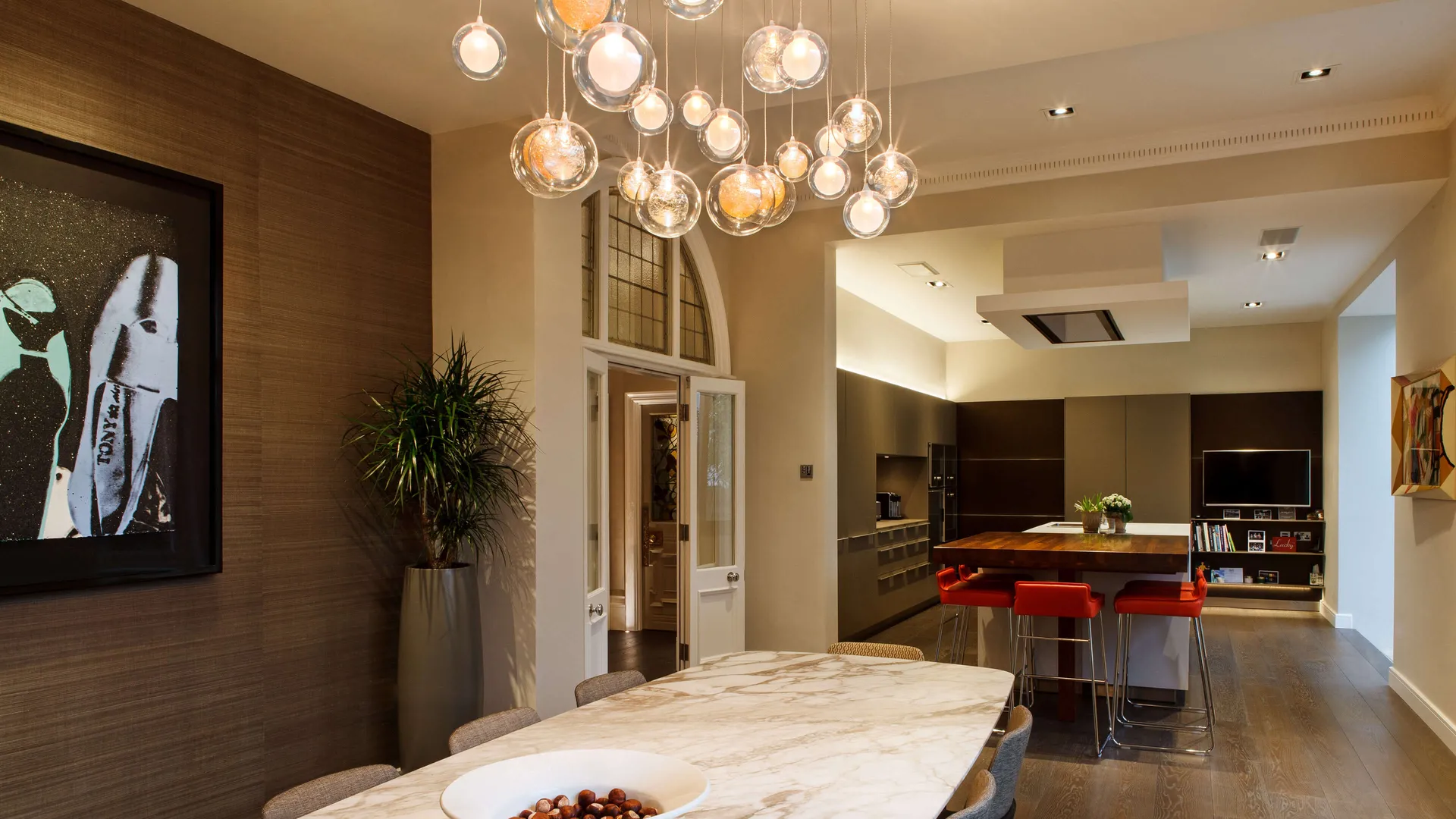 Custom chandelier over a dining table and a sleek modern kitchen with LED linear lighting and powerful downlights