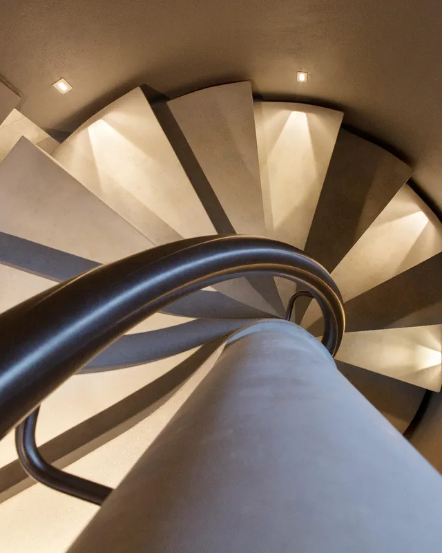 Top-down view of a spiral staircase lit with small, thin wall-mounted accent lights