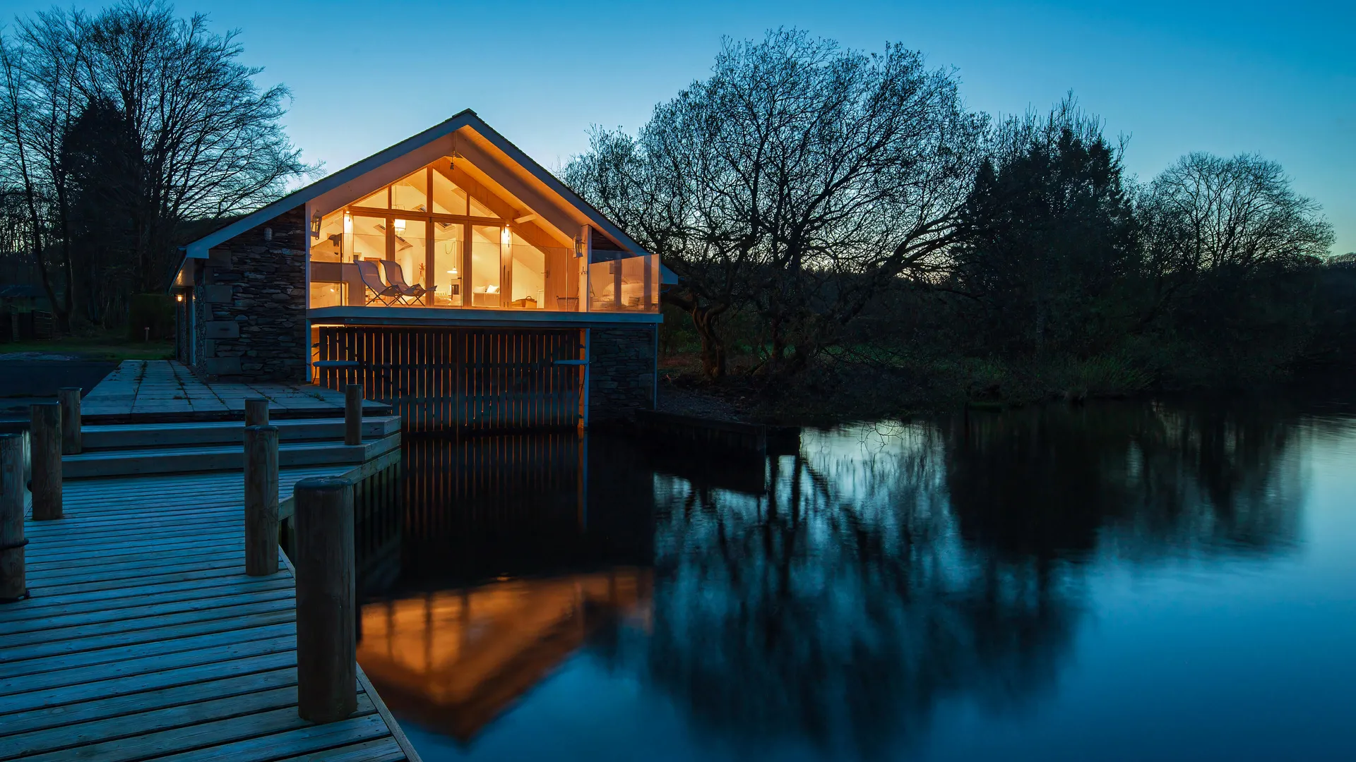 A beautiful Lakeland boathouse on a lake, lit up in the early evening