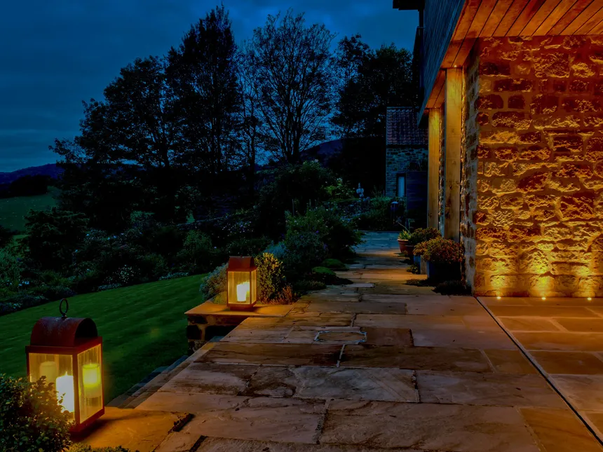 Lanterns and up and down lighting on the pathway leading down to the lawn in a lighting design for a new-build house in a lovely setting