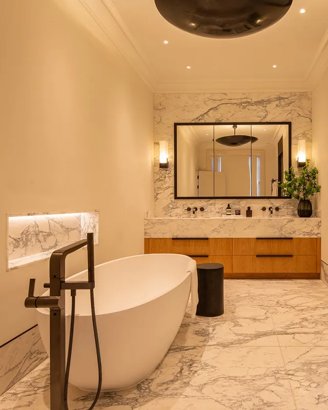 A sleek, modfern bathroom with downlights, mirror lighting and a lit niche by the freestanding bath