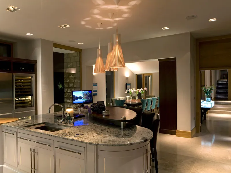 A modern kitchen in the foreground with pendant lighting over the island and accent lighting in the background..  