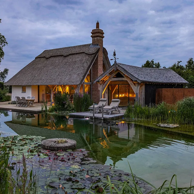 Subtle warm lighting for an oak-framed pool house by a swimming lake