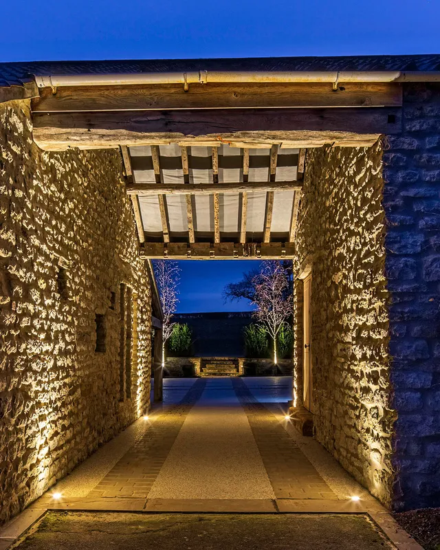 A stone arch with ground recessed uplighting and garden lighting beyond