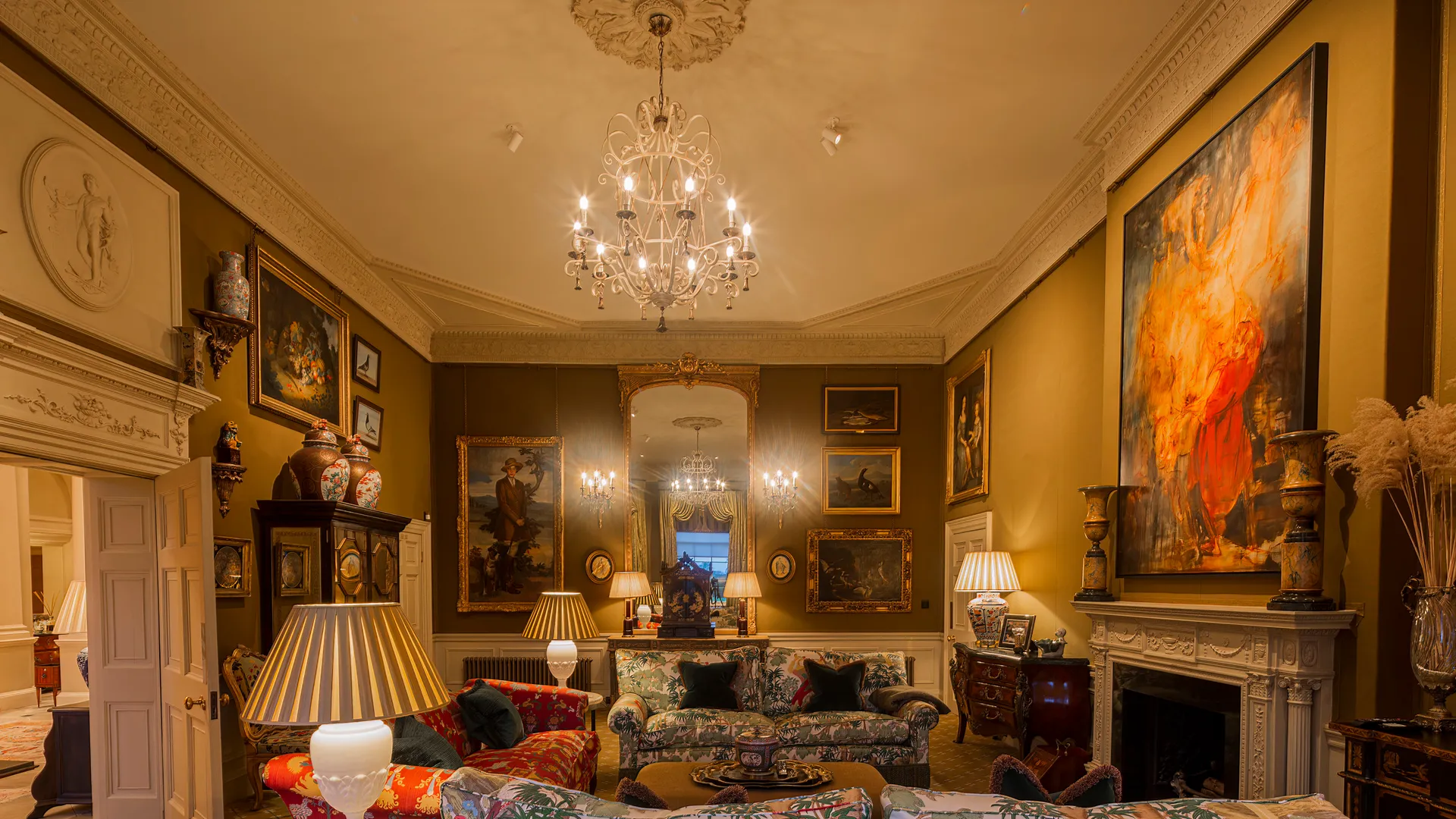 Lighting for a grand staircase and hallway in an English country house with chandeliers, picture lights and table lamps