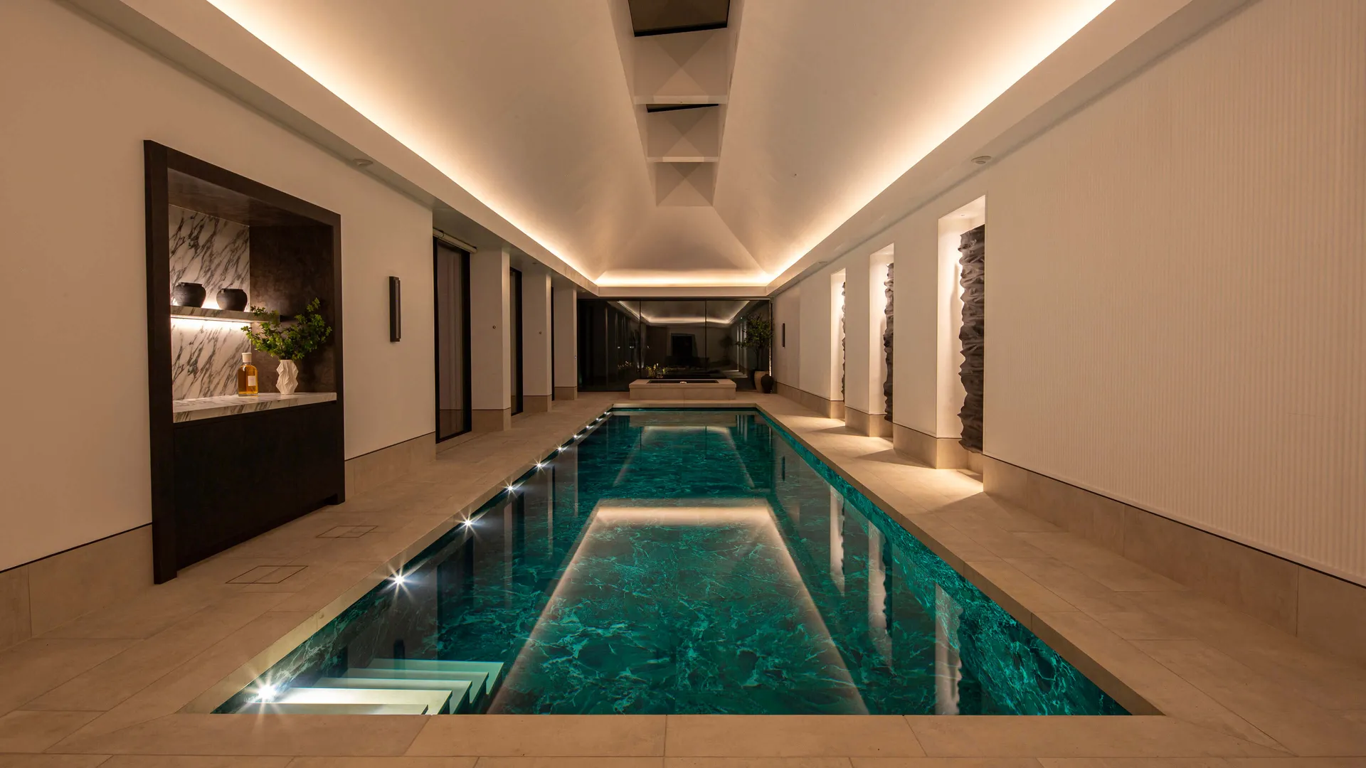 A beautifully tiled swimming pool with coffer lighting in a pitched ceiling