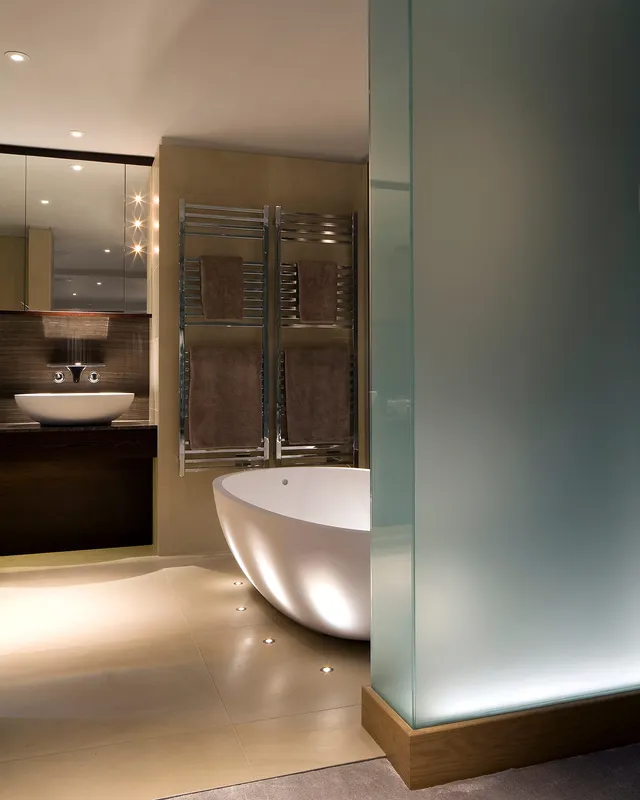 Glamorous bathroom with an uplit ovoid bath and frosted glass wall 