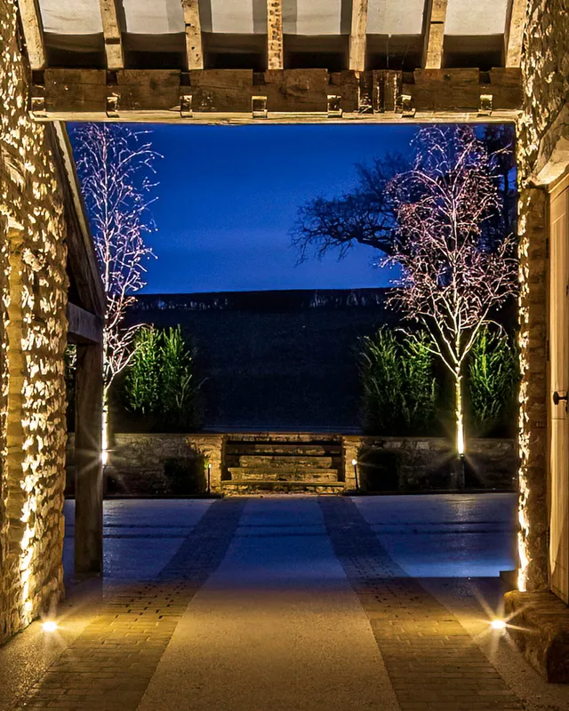 Looking through a lit stone arch to a focal point of garden steps framed by uplit Silver Birch