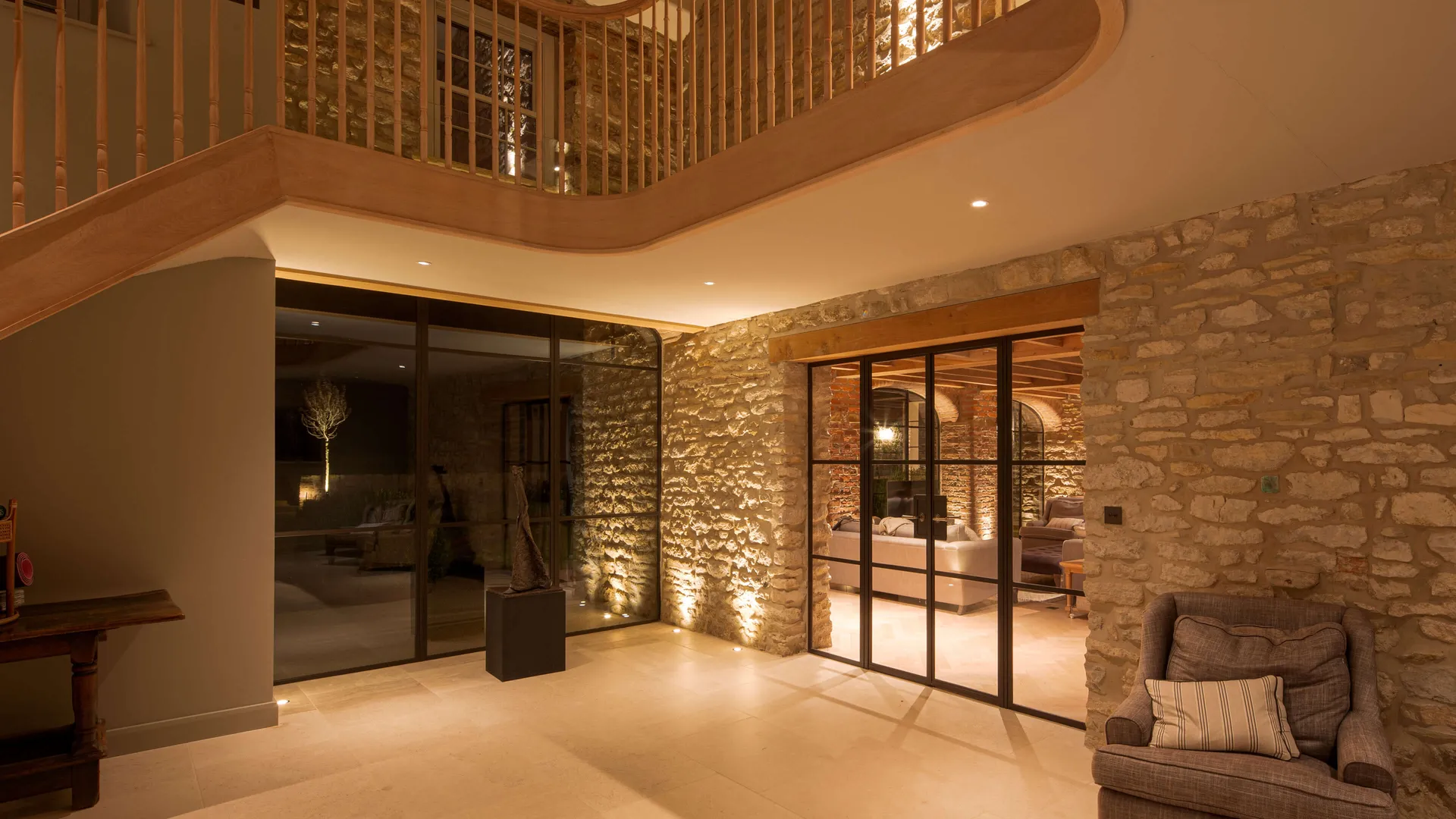 lighting for a double height staircase with uplit stone walls and lighting for feature trees in the garden beyond