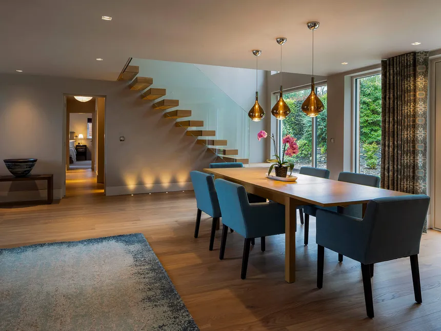 A modern dining room with pendants over the dining table and a moden cantilever staircase underlit with LED.